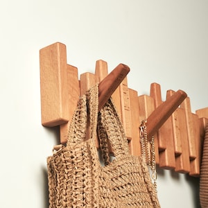 May include: A wooden wall-mounted coat rack with multiple hooks, featuring a straw tote bag hanging from one of the hooks.