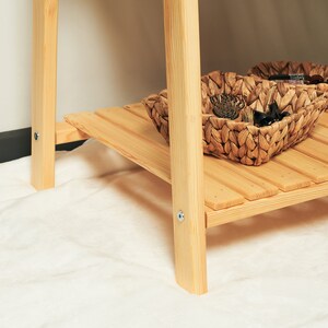 May include: A wooden shelf unit with two shelves and a woven basket on the bottom shelf.