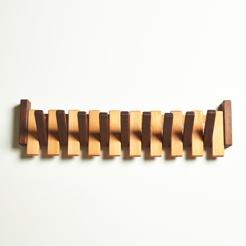 Peut inclure: Un porte-manteau en bois avec 16 crochets. Les crochets sont dispos&eacute;s en quinconce et sont faits de deux teintes de bois diff&eacute;rentes, brun et brun clair.