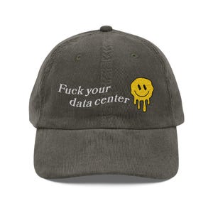 May include: Dark olive green corduroy baseball cap. The cap features the embroidered text "Fuck your data center" in white, and a yellow, smiling face with dripping details.