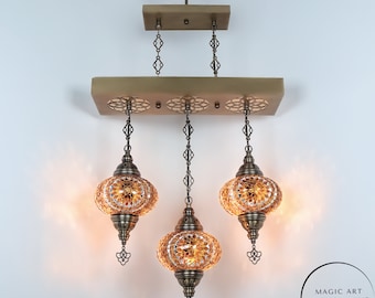 May include: A three-light chandelier with amber glass mosaic shades and a brass finish. The chandelier has a wooden base with a decorative pattern. The text "MAGIC ART TURKISH LAMP Mosaic Lights" is visible in the bottom right corner of the image.