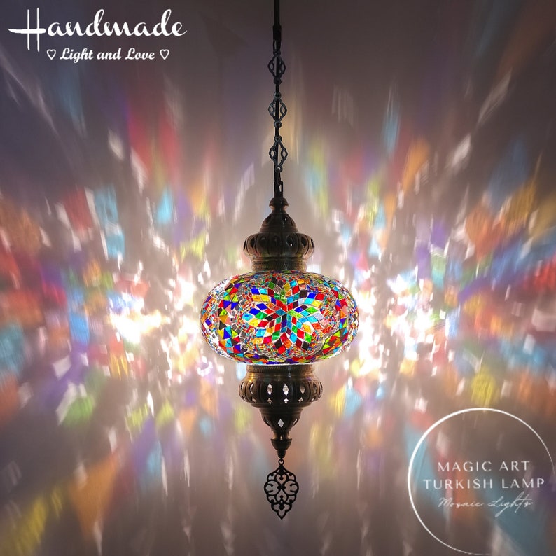 May include: A colorful Turkish mosaic glass lamp with a round shape and a metal chain hanging from the ceiling. The lamp is lit and casting a rainbow pattern on the ceiling. The text "MAGIC ART TURKISH LAMP Mosaic Lights" is visible in the bottom right corner of the image.