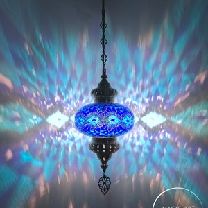 May include: A blue mosaic Turkish lamp with a metal chain hanging from the ceiling. The lamp casts a colorful light pattern on the ceiling. The text "MAGIC ART TURKISH LAMP Mosaic Lights" is visible in the lower right corner of the image.