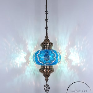 May include: A turquoise blue Turkish mosaic glass lamp with a brass chain and ornate brass accents. The lamp is hanging from a ceiling fixture. The text "MAGIC ART TURKISH LAMP Mosaic Lights" is visible in the lower right corner of the image.