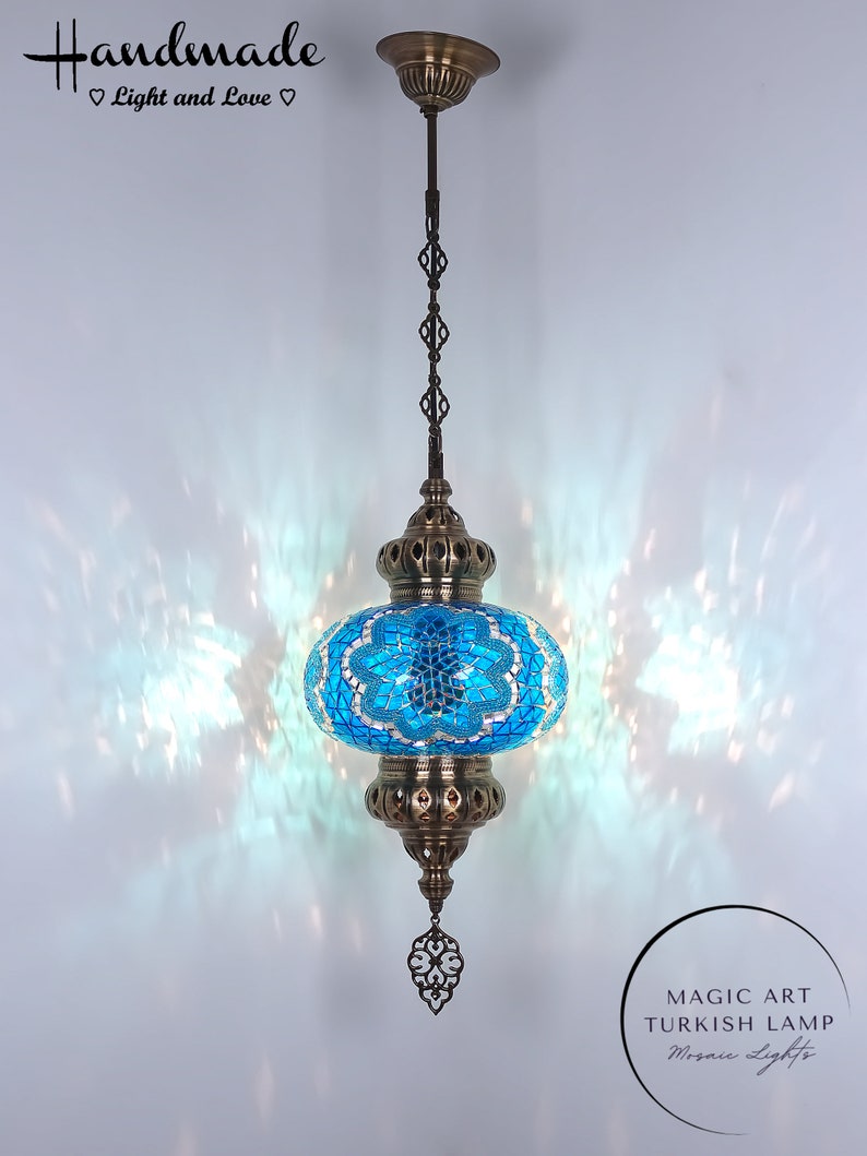 May include: A turquoise blue Turkish mosaic glass lamp with a brass chain and ornate brass accents. The lamp is hanging from a ceiling fixture. The text "MAGIC ART TURKISH LAMP Mosaic Lights" is visible in the lower right corner of the image.