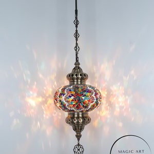 May include: A colorful mosaic Turkish lamp with a brass finish and a decorative chain hanging from the ceiling. The lamp is lit and casting a warm glow. The text "MAGIC ART TURKISH LAMP Mosaic Lights" is visible in the lower right corner of the image.