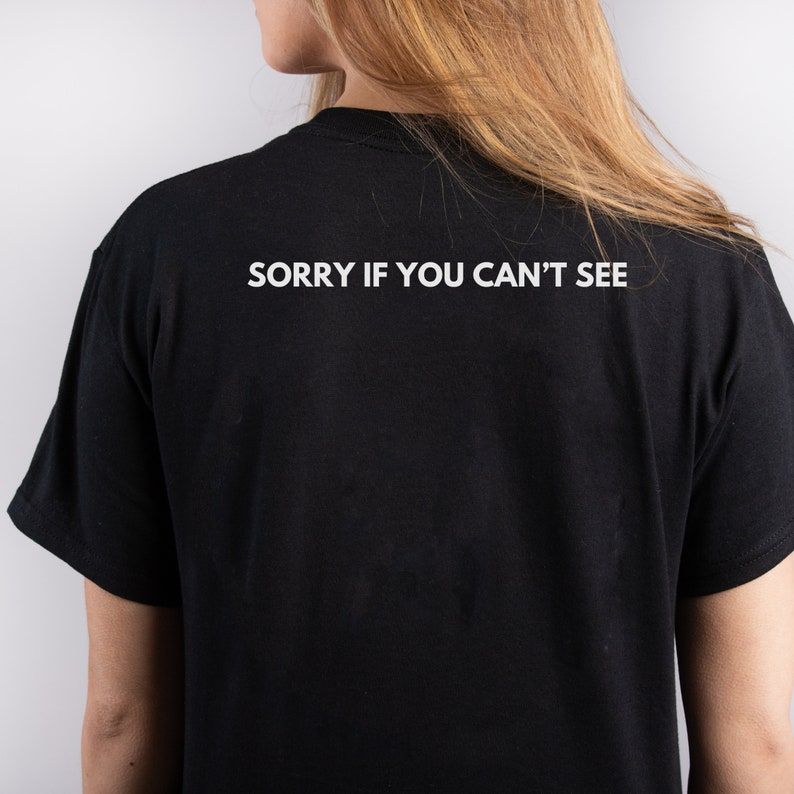 Puede incluir: Camiseta negra con el texto blanco "SORRY IF YOU CAN'T SEE" impreso en la espalda. La camiseta est&aacute; hecha de un material suave y es una prenda informal.