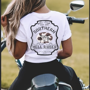 May include: White t-shirt with a black and white graphic design of a skull with antlers and the text "Southern Est. 1999 Hell Raiser".