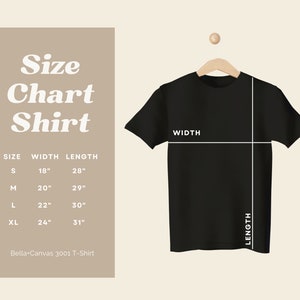 Puede incluir: Una camiseta negra colgada de una percha de madera, con l&iacute;neas blancas que indican el ancho y el largo. Una tabla de tallas a la izquierda muestra las medidas en cm: S (45,7cm ancho, 71,1cm largo), M (50,8cm ancho, 73,7cm largo), L (55,9cm ancho, 76,2cm largo), XL (61cm ancho, 78,7cm largo).