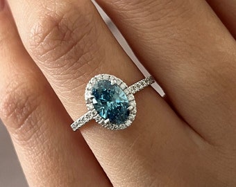 May include: A silver ring featuring a large oval blue gemstone with a halo of smaller diamonds.