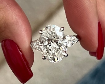 May include: A silver ring with a large oval-shaped diamond and two smaller pear-shaped diamonds on either side.