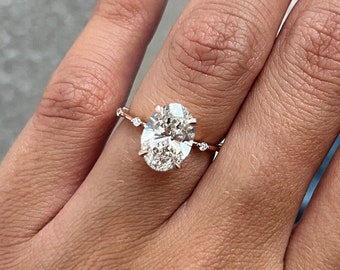 May include: A close-up of a hand wearing a rose gold engagement ring with an oval-shaped diamond. The ring has small diamonds set on the band.