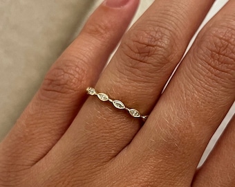 May include: A delicate gold ring with a row of small, clear, oval-shaped stones.