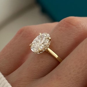 May include: A gold engagement ring with an oval-shaped diamond center stone and a halo of smaller diamonds.