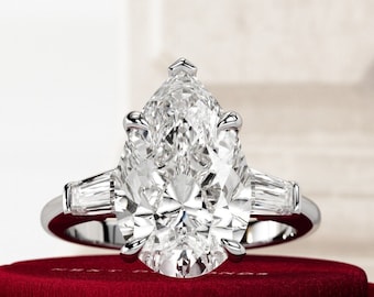 May include: A pear-shaped diamond engagement ring with a silver band and two smaller baguette diamonds on either side of the center stone.
