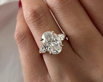 May include: A gold ring featuring a large oval-shaped diamond with two smaller pear-shaped diamonds flanking it.