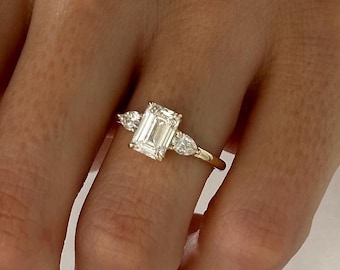 May include: A gold ring with a large emerald-cut diamond and two smaller pear-shaped diamonds on either side.