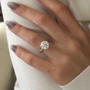 Pu&ograve; includere: Primo piano di una mano che indossa una fascia d'oro con un grande anello di diamanti rotondi e trasparenti.