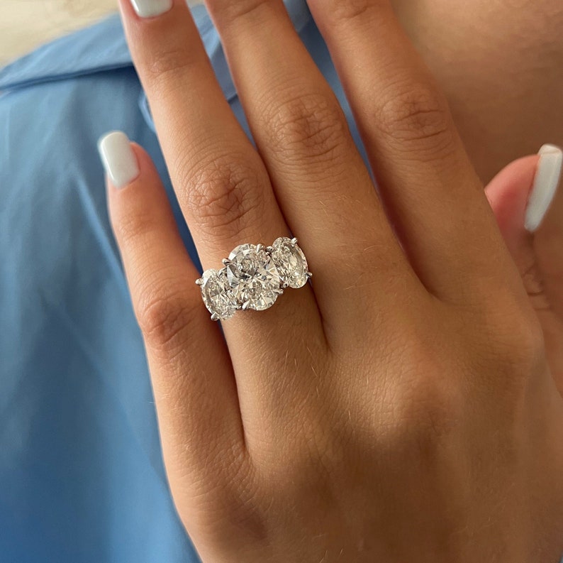 Puede incluir: Un anillo de plata con tres diamantes grandes de forma ovalada engastados en fila.