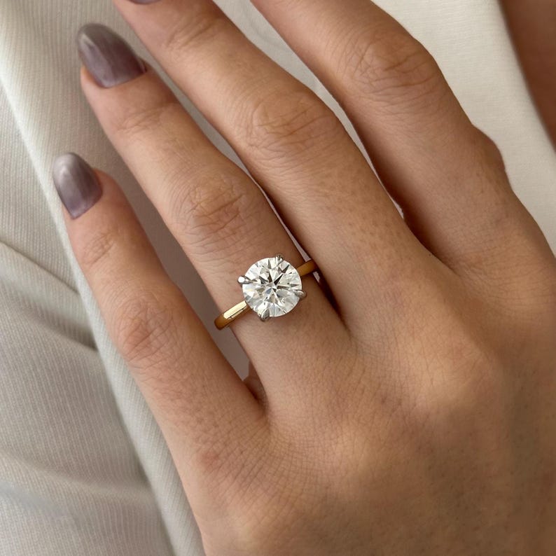 Pu&ograve; includere: Un anello di fidanzamento in oro con un grande diamante rotondo e chiaro.