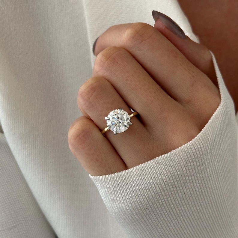 Pu&ograve; includere: Un anello di fidanzamento in oro con un grande diamante rotondo e chiaro.