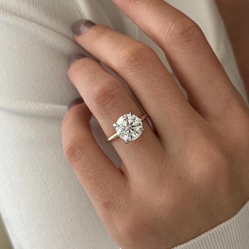 Pu&ograve; includere: Un anello di fidanzamento in oro con un grande diamante rotondo e chiaro.