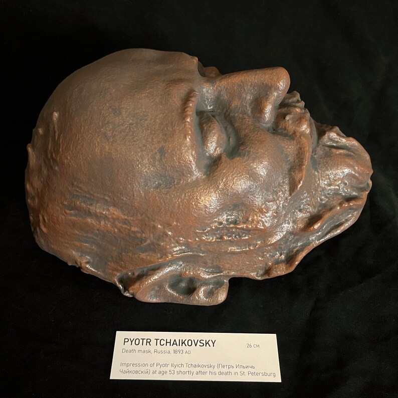Puede incluir: Una m&aacute;scara mortuoria de bronce de Piotr Ilich Chaikovski, creada en Rusia en 1893. La m&aacute;scara mide 26 cm de largo y muestra el rostro del compositor poco despu&eacute;s de su muerte. La m&aacute;scara se exhibe sobre una superficie oscura.
