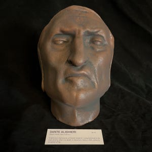 May include: A weathered, brown sculpture of a human head, likely a death mask. The sculpture has a somber expression and is approximately 26 cm in height. A label at the base identifies it as a traditional impression of Dante Alighieri.