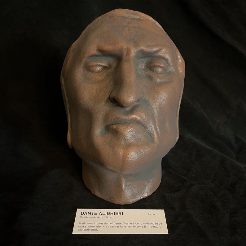 May include: A weathered, brown sculpture of a human head, likely a death mask. The sculpture has a somber expression and is approximately 26 cm in height. A label at the base identifies it as a traditional impression of Dante Alighieri.
