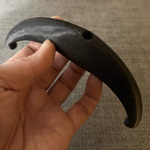 May include: A black plastic handle with a hole in the centre. The handle is curved and has a smooth surface.