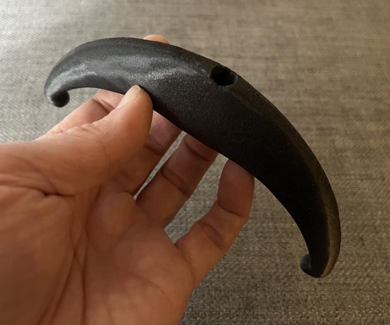 May include: A black plastic handle with a hole in the centre. The handle is curved and has a smooth surface.