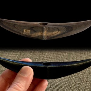 以下が含まれることがあります： 三日月形の石の道具が2つ。1つは自然な茶色と黒の仕上げ、もう1つは黒の仕上げ。両方の道具の中央に穴が開いています。