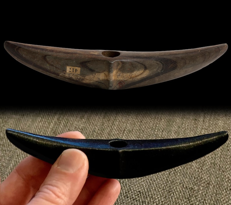 以下が含まれることがあります： 三日月形の石の道具が2つ。1つは自然な茶色と黒の仕上げ、もう1つは黒の仕上げ。両方の道具の中央に穴が開いています。