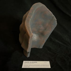 May include: A sculpted effigy of Dante Alighieri, a death mask from Italy, 1321. The sculpture is a muted gray and brown color. The text on the card reads "DANTE ALIGHIERI" and "26 cm".