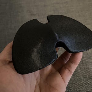 May include: A black, 3D printed, curved, geometric shape with a hole in the center.