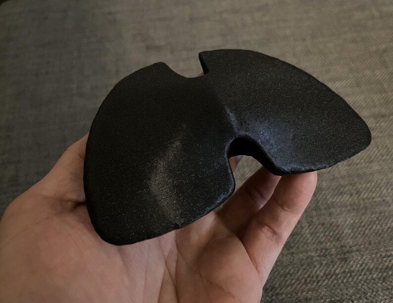 May include: A black, 3D printed, curved, geometric shape with a hole in the center.