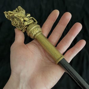 May include: An antique-style walking stick, featuring a gold-toned decorative top with a lion and shield motif. The handle is cylindrical, leading to a dark shaft. The design suggests a vintage or historical origin.