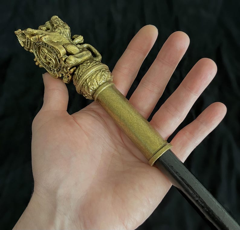 May include: An antique-style walking stick, featuring a gold-toned decorative top with a lion and shield motif. The handle is cylindrical, leading to a dark shaft. The design suggests a vintage or historical origin.