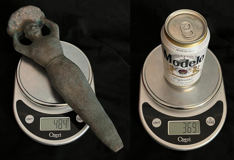 May include: Two digital kitchen scales with a bronze-colored statue of a woman on one scale and a can of Modelo Especial beer on the other scale. The scales display the weight of each item in ounces.