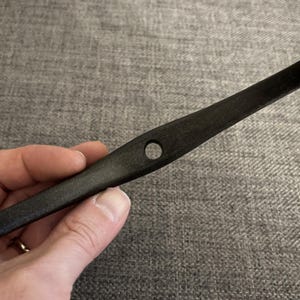 May include: A black wooden tool with a hole in the centre. The tool is curved and has a rounded end.