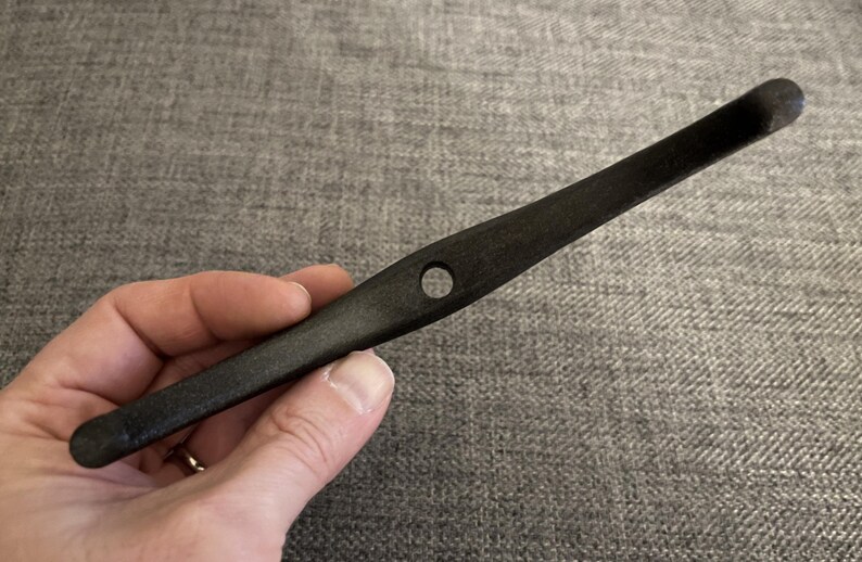 May include: A black wooden tool with a hole in the centre. The tool is curved and has a rounded end.
