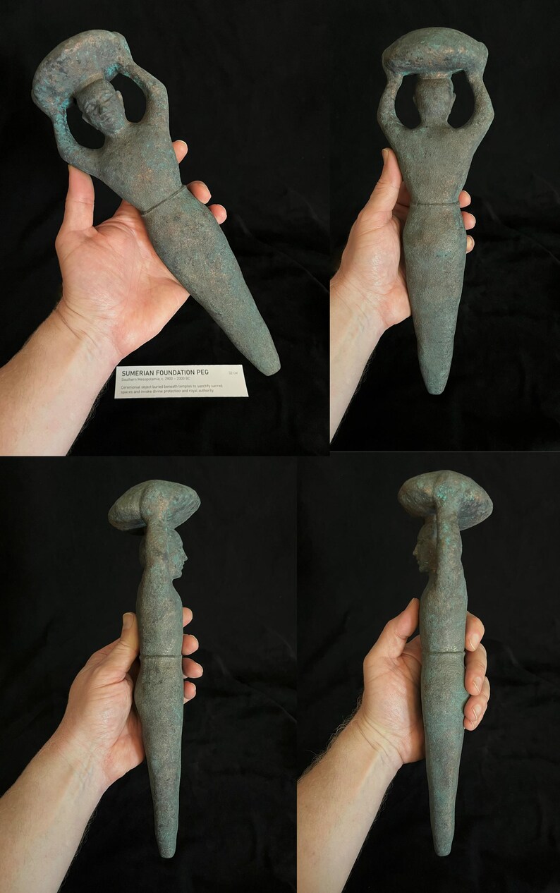 May include: A green stone sculpture of a figure holding a round object above their head. The sculpture is about 15 inches tall and is made of a smooth, green stone. The figure is standing on a pedestal and is wearing a long, flowing robe. The sculpture is a Sumerian foundation peg, also known as a "peg-figurine".