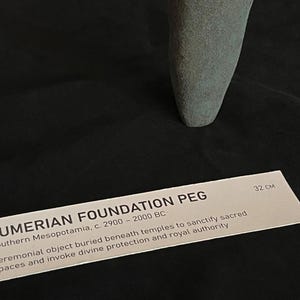 May include: A gray stone Sumerian foundation peg, approximately 32 cm long. It is a ceremonial object buried beneath temples to sanctify sacred spaces and invoke divine protection and royal authority. Southern Mesopotamia, c. 2900-2000 BC.