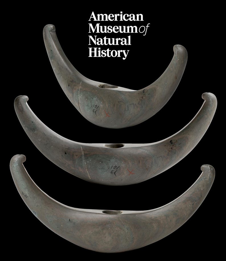May include: Three grey stone crescent-shaped objects with a hole in the centre. The objects are stacked on top of each other. The objects are labelled with the text "American Museum of Natural History".