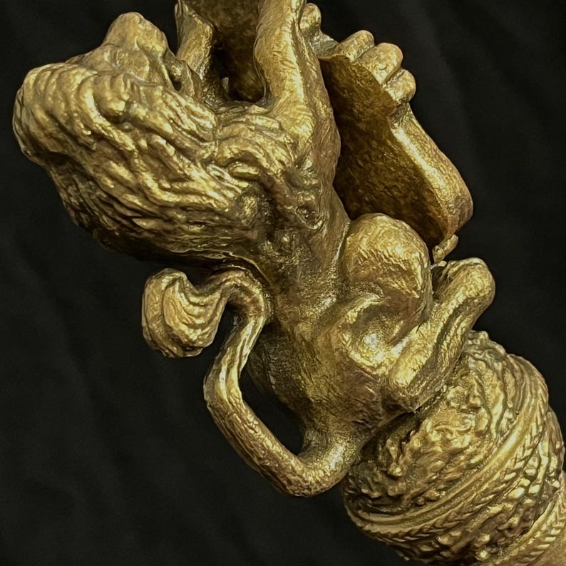 May include: A detailed, gold-coloured sculpture of a mythical creature. The sculpture features intricate details, including textured surfaces and a decorative base. The creature appears to be holding an object. The background is a solid black.