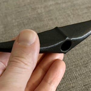以下が含まれることがあります： 中央に穴が開いた湾曲した刃を持つ黒いプラスチック製のツール。ツールは手で持たれています。
