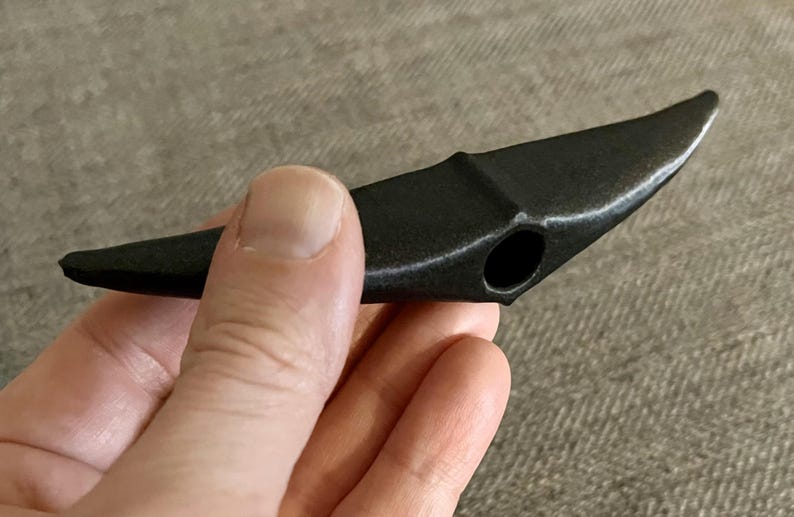 以下が含まれることがあります： 中央に穴が開いた湾曲した刃を持つ黒いプラスチック製のツール。ツールは手で持たれています。