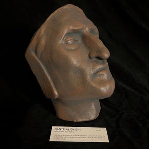 May include: A bronze-colored sculpted death mask of Dante Alighieri. The mask is a side profile with a prominent nose and detailed facial features. A label reads "DANTE ALIGHIERI Death mask, Italy, 1321 AD" and "26 CM".