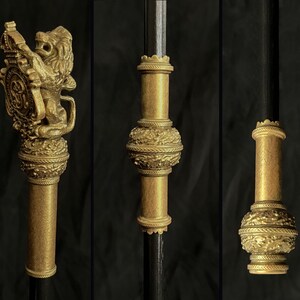May include: Ornate gold-coloured staff with detailed designs. The staff has a lion holding a shield, and other sections with floral and geometric patterns. The staff is set against a dark background.