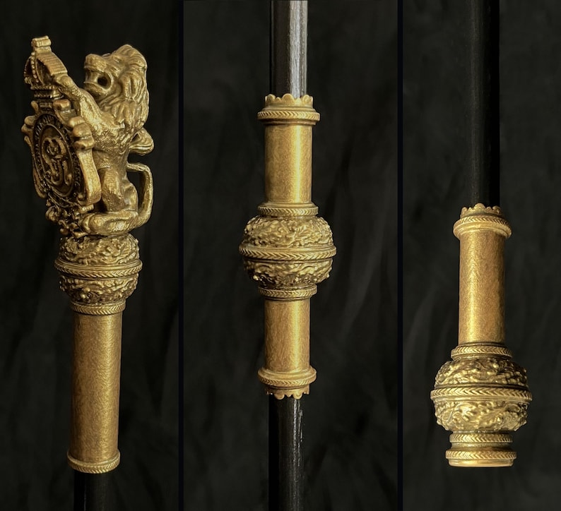 May include: Ornate gold-coloured staff with detailed designs. The staff has a lion holding a shield, and other sections with floral and geometric patterns. The staff is set against a dark background.
